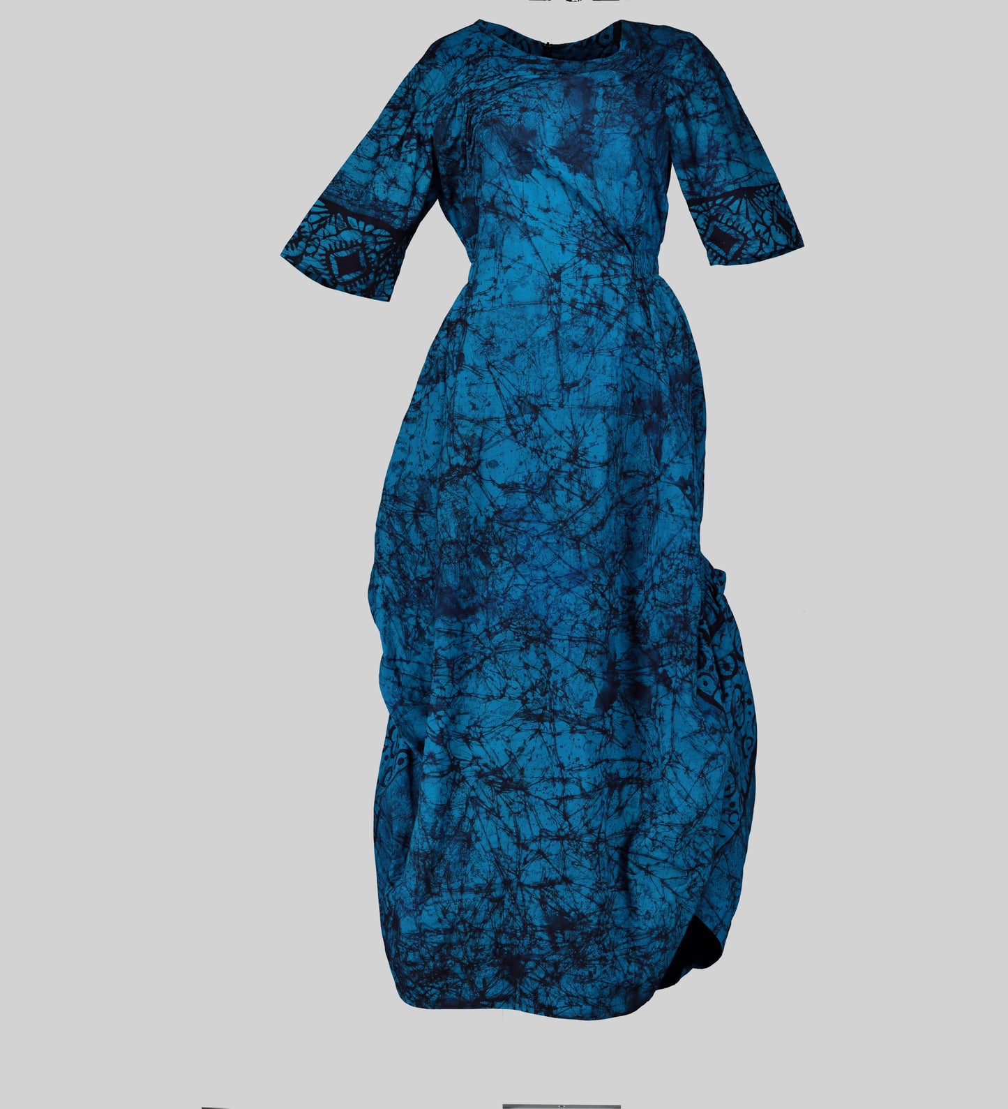 A long African wax print maxi dress with a vibrant blue colorway and intricate geometric patterns. The dress features a flattering ruched bodice and a comfortable round neckline.