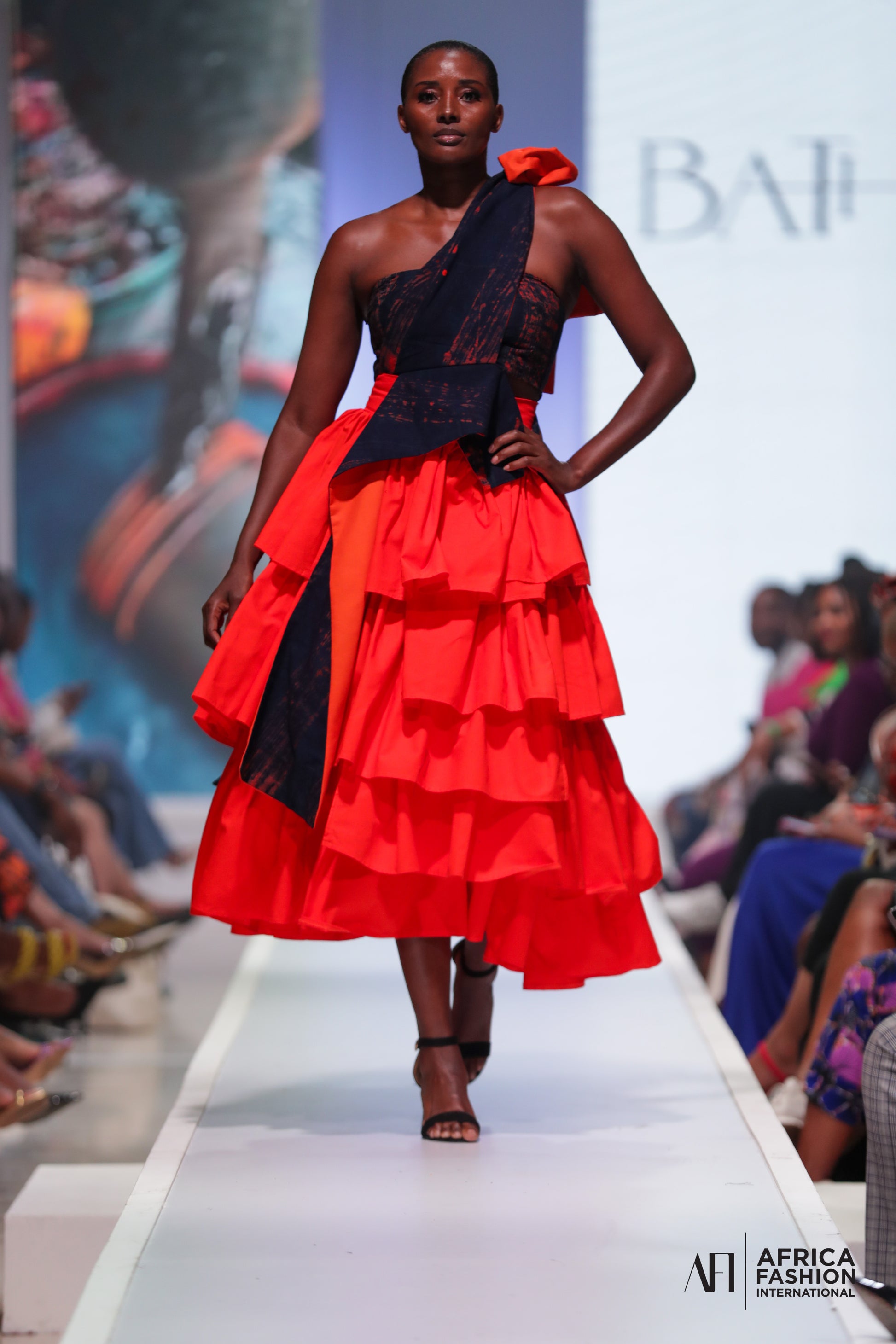 Model wearing the orange NTOBEKO XIBELANI SKIRT by Bathini Kowane, showcasing its movement and asymmetrical design.